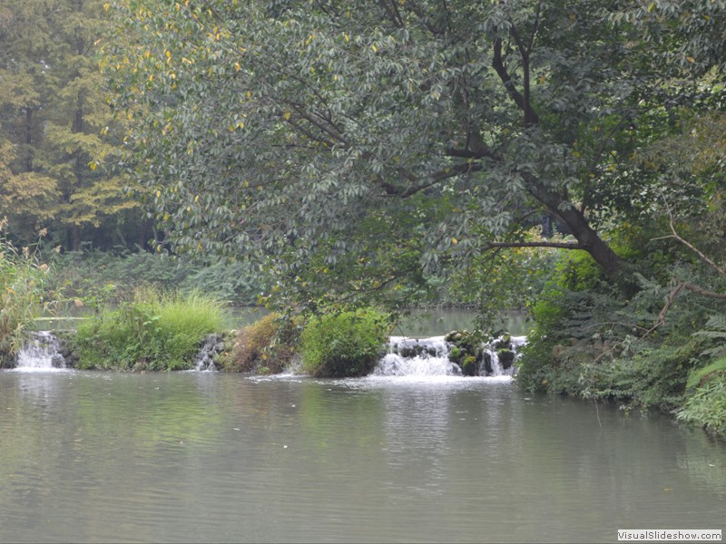 A small water fall flowing between the ponds in the park.