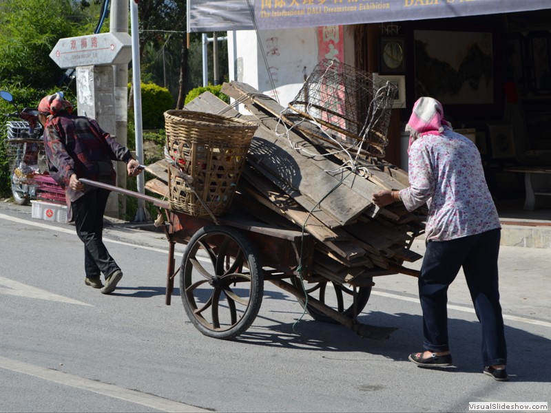 A couple of women moving their heavy load through town.